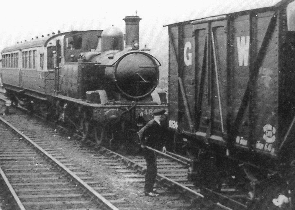 Close up showing the mixed train being assembled by the station porter who is standing ready to couple up the van