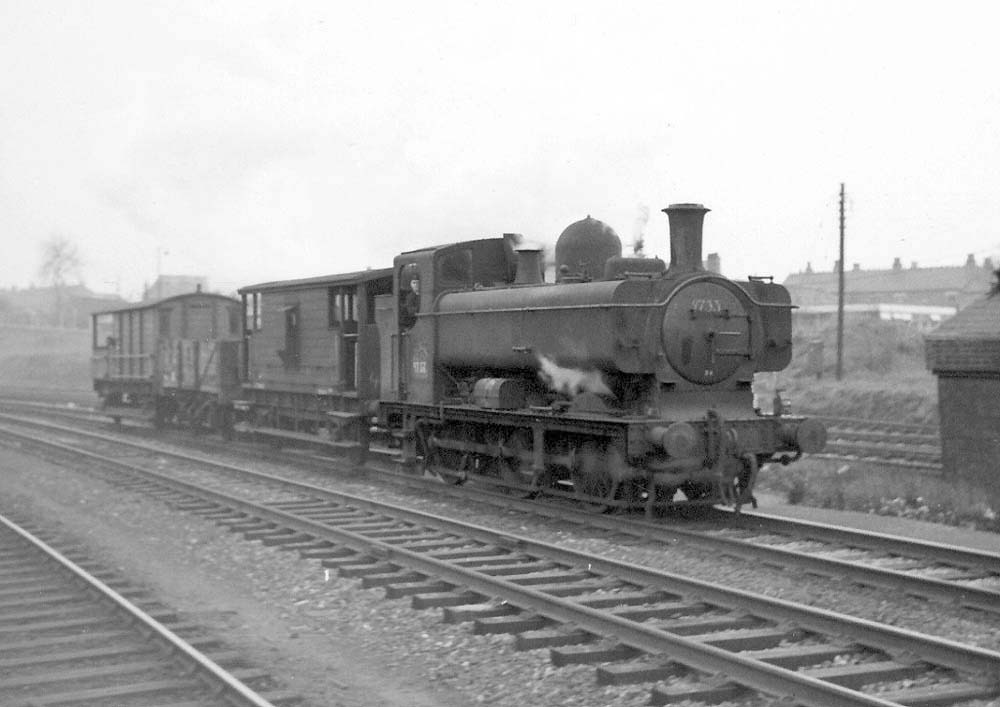 Ex-GWR 0-6-0PT No 9753 is seen at the head of a short train of two gaurds van with an open truck in between on 15th February 1965
