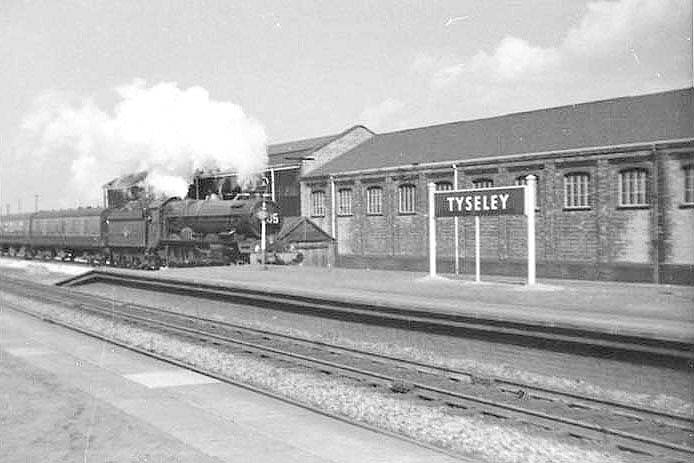 An unidentified ex-GWR 4-6-0 King class locomotive is seen passing through Tyseley station's up main platform with an express service to Paddington