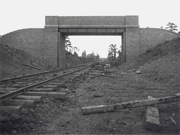 A single line of contractor's temporary track passes beneath a brick and girder overbridge