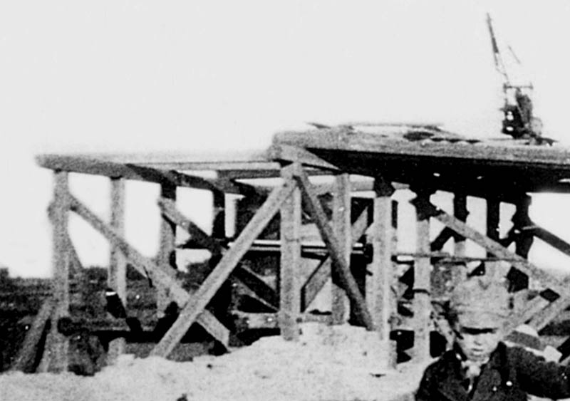 Close up of the opposite end of the temporary timber bridge showing a smaller derrick in place and a partially built abutment