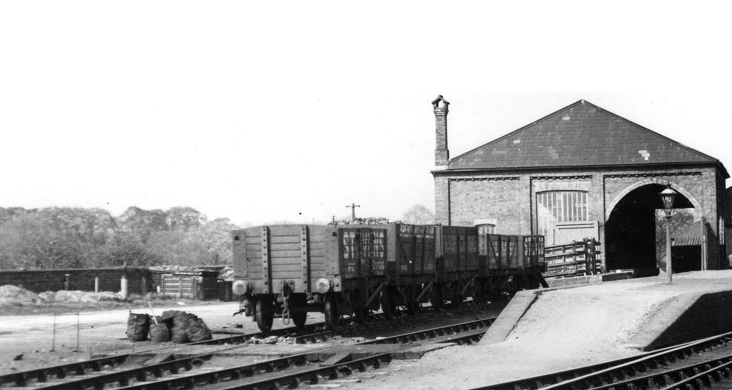 Close up showing the goods shed and a rake of five open mineral wagons standing in front of the cattle dock