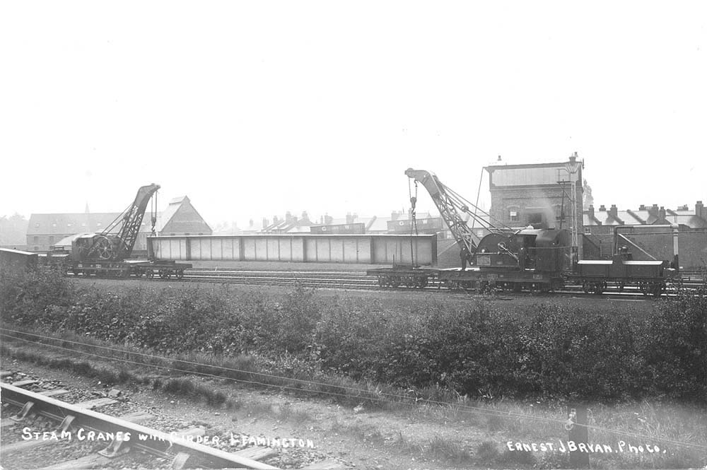A pair of GWR steam cranes, with a girder suspended between them, are seen stabled in the carriage sidings alongside Leamington Engine shed circa 1906