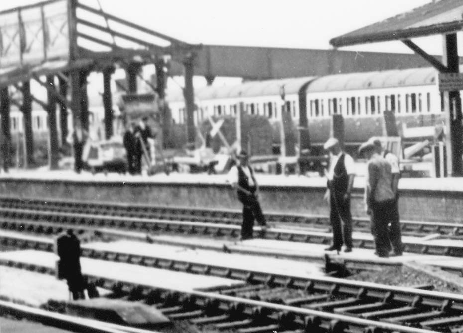 Close up showing workmen laying timber planking to the track and track bed between the up and down platforms