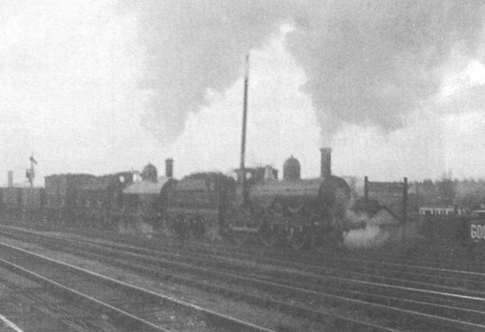 A GWR 2-4-0 pilots a GWR 0-6-0 on a lengthy up goods train towards the goods loop at the rear of the station