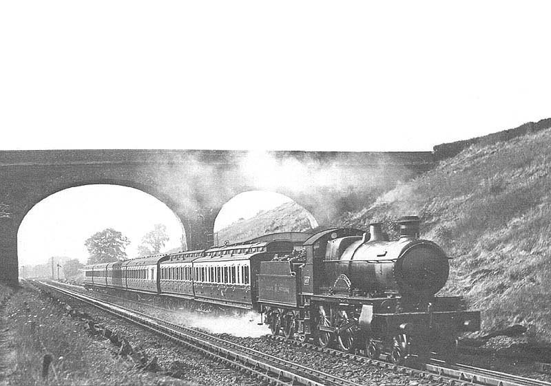 An unidentified GWR 4-4-0 County Class locomotive hauling a rake of mixed coaching stock passes over Rowington troughs on an up service