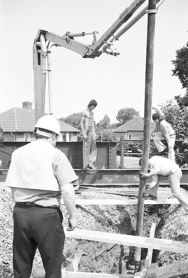 View of railway workers placing concrete into the abutment of Wharf Street bridge via a concrete pump