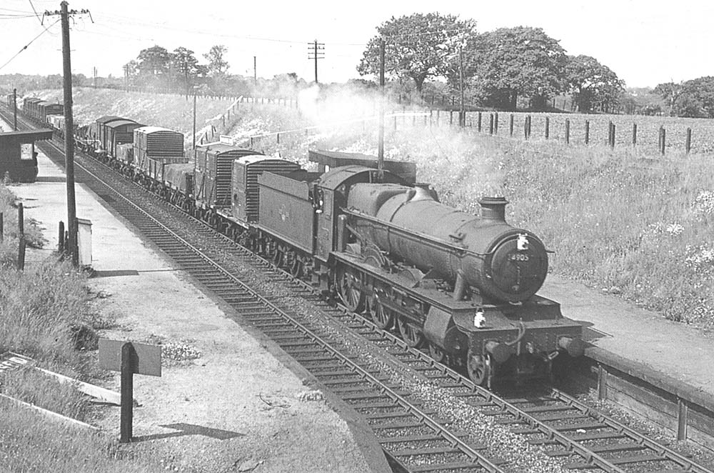 Ex-GWR 4-6-0 Hall class No 4905 'Barton Hall' is seen passing through Whitlock End Halt at the head of an up Class D express freight service to Birmingham