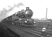 GWR 4-6-0 No 6014 'King Henry VII' is seen on an up express with a Siphon G van behind the tender as it passes alongside the goods yard