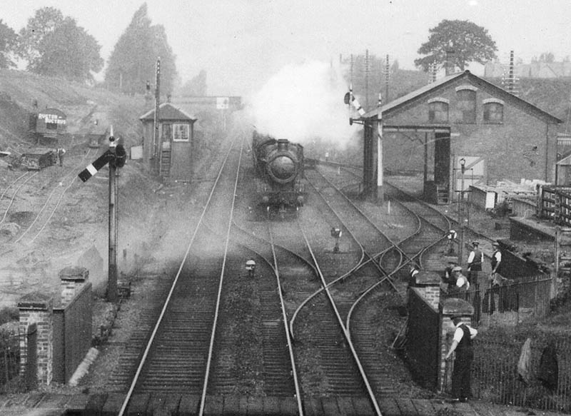 Close up showing the signal box and goods shed and yard whilst an unknown GWR 4-6-0 storms past the signal