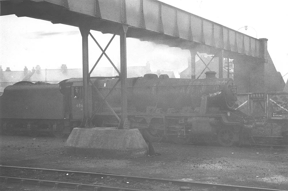 An unidentified ex-LMS 8F 2-8-0 locomotive is seen standing beneath the footbridge crossing Gosford Green goods yard
