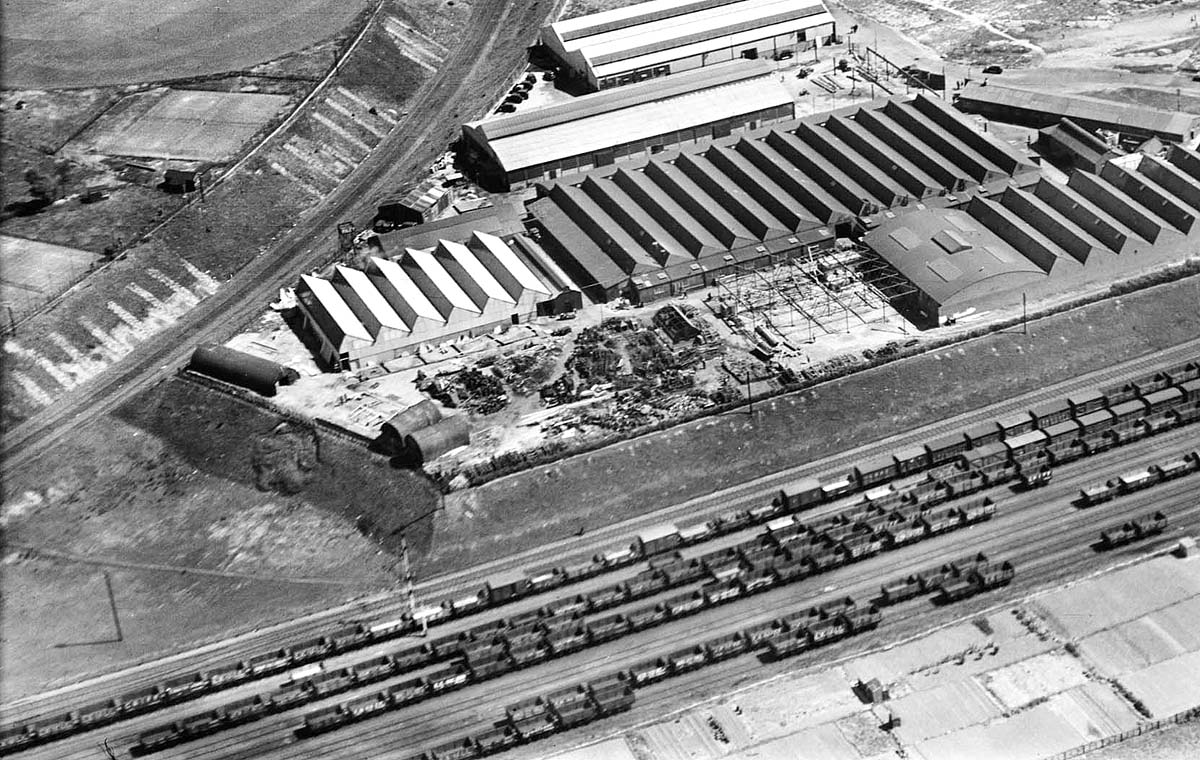 An aerial view showing a goods train comprised of open wagons and vans is passing the signals at Three Spires Junction