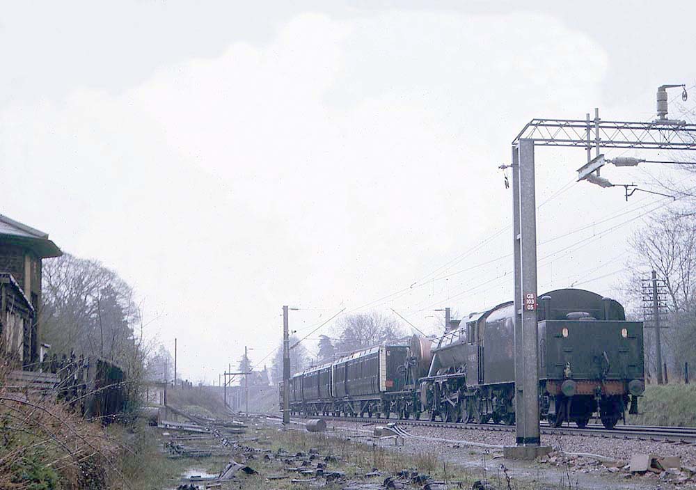 An unidentified ex-LMS 2-8-0 8F locomotive runs tender, first wrong line, with an electrification train on 23rd April 1966