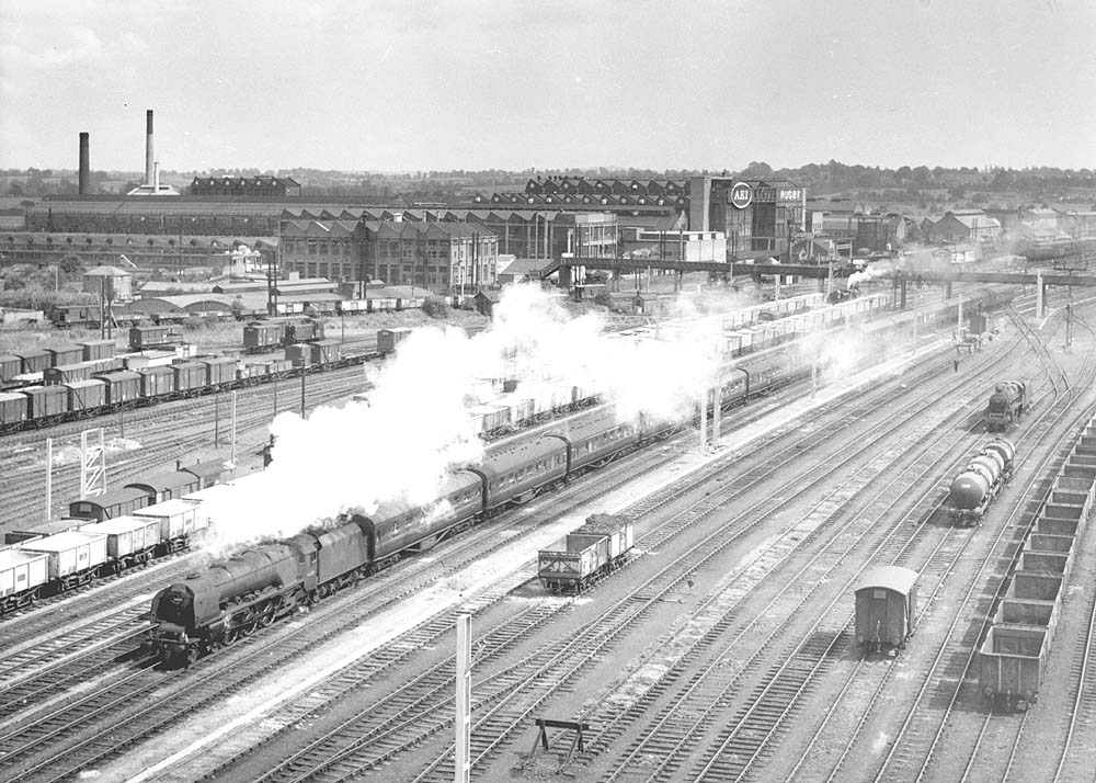 An unidentified ex-LMS 8P 4-6-2 Coronation Class locomotive at the head of a down express passes the up marshalling sidings