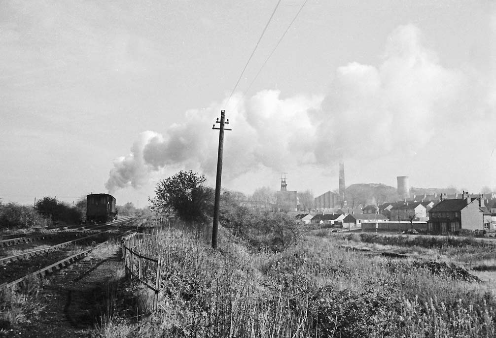 An unidentified ex-LMS 2-8-0 8F locomotive is seen coupled to a brakevan as it ascends the bank past Kingsbury Colliery