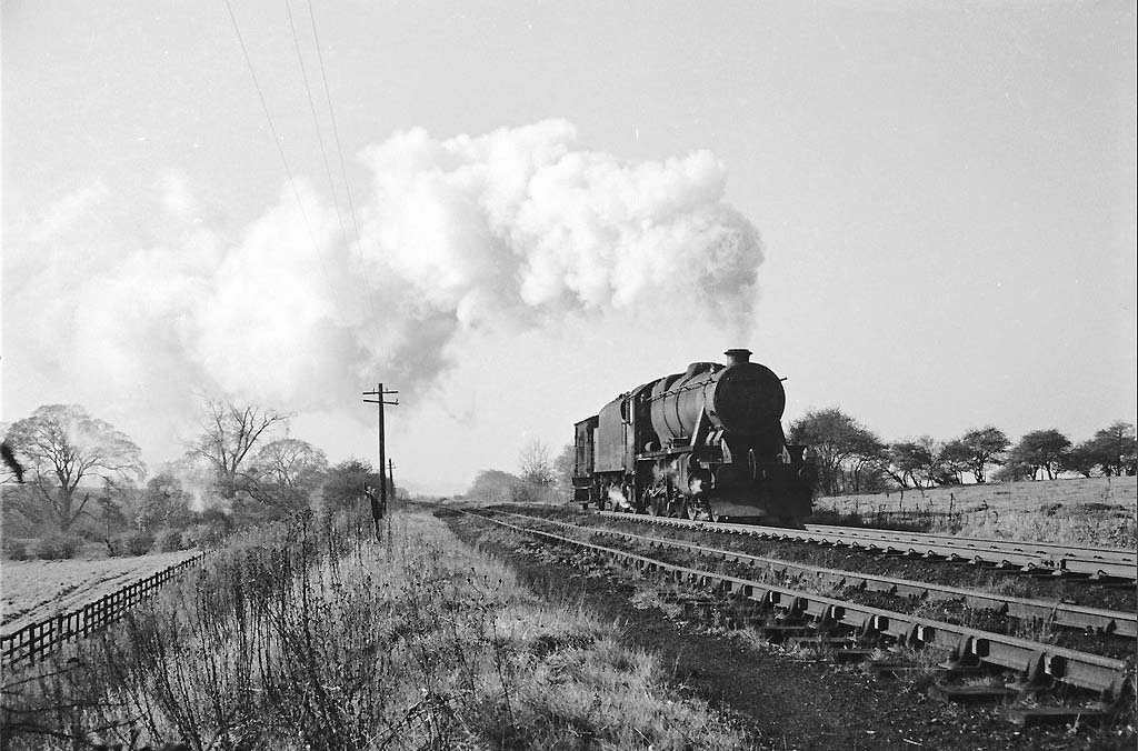 An unidentified ex-LMS 2-8-0 8F locomotive is seen coupled to a brakevan as it approaches the bank past Kingsbury Colliery