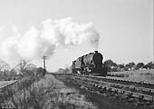 An unidentified ex-LMS 2-8-0 8F locomotive is seen coupled to a brakevan as it approaches the bank past Kingsbury Colliery