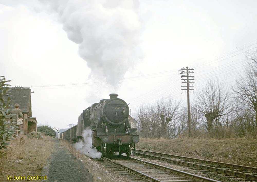 Ex-LMS 8F 2-8-0 No 48474 is seen passing through Ettington station's up platform with a down mineral train on 20th February 1965