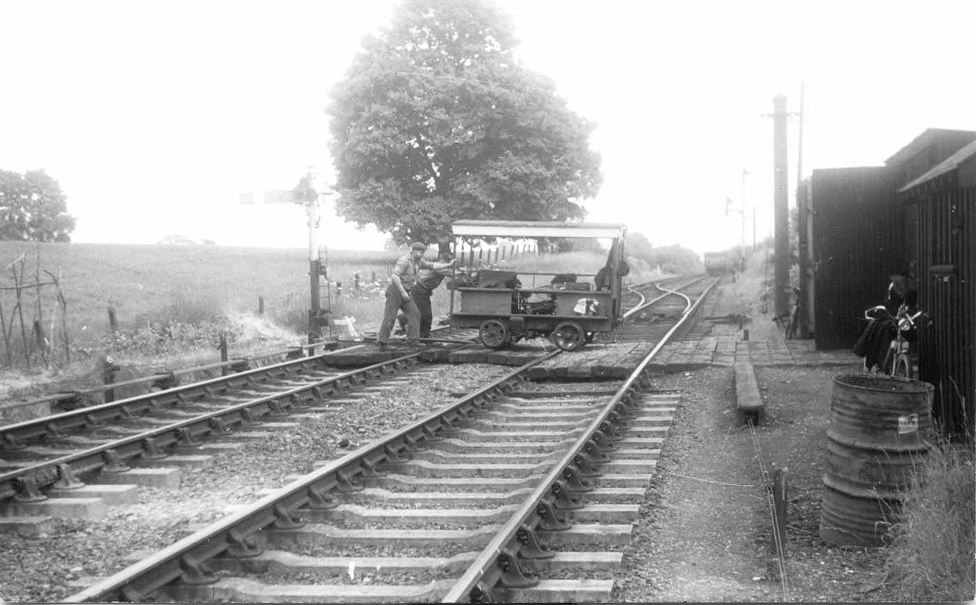 A motorised trolley used by the Permanent Way gang is being manhandled across the running lines at Byfield in 1958