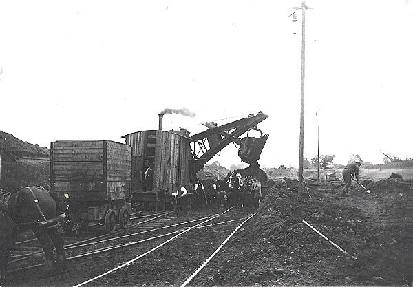 One of the many steam shovel's in action tipping its load into a horse drawn contractors wagon